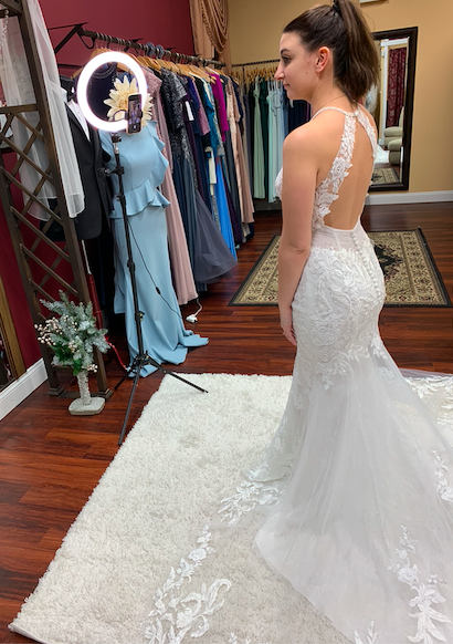 Bride in a mermaid lace wedding dress with a keyhole back using a ring light to share the dress details over the phone with her family who participated in the video appointment from home
