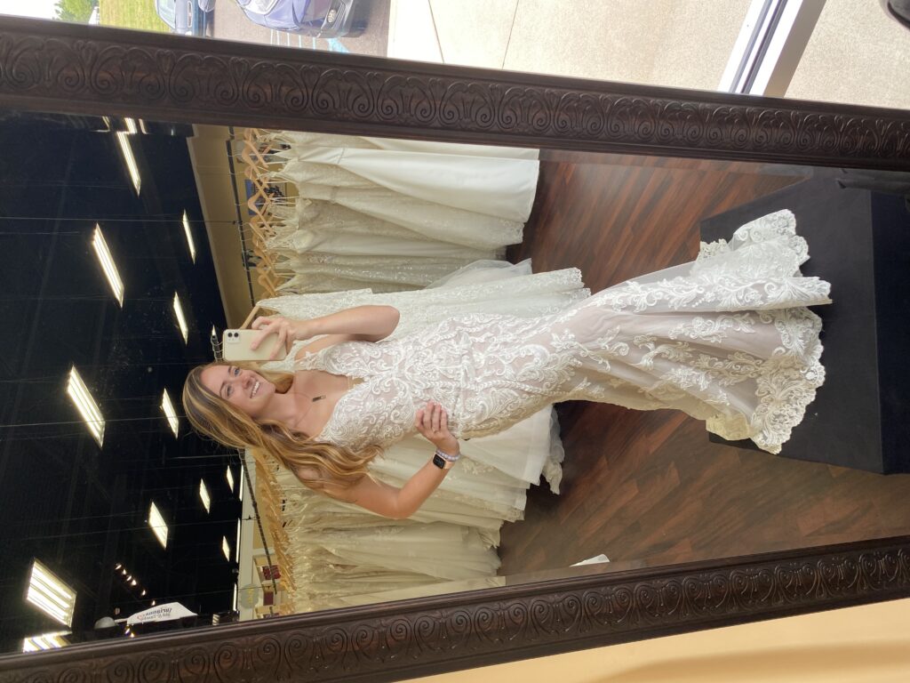 Tori in a Madi Lane fit and flare lace dress taking a selfie in the mirror at Darianna Bridal & Tuxedo