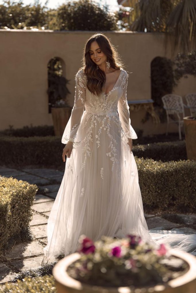 lace wedding dress harkening back to the 1970s with long sheer sleeves, flowy and light tulle skirt, fully open back, scattered vine patterned lace
