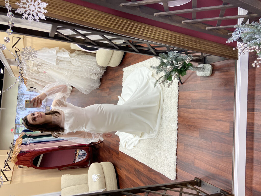 Bride modeling the Aiden dress, Madi Lane, crepe wedding dress, square neck, tank strap, sheer jacket over lay with pearls, micro wedding dress