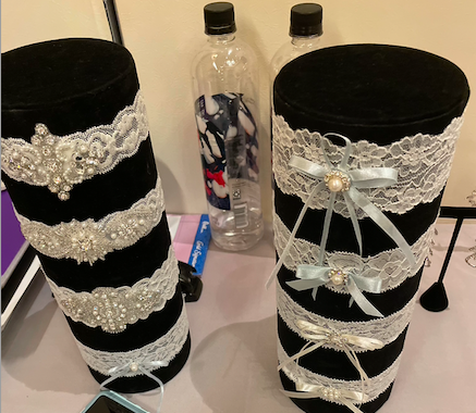 wide pearl and crystal beaded bridal belts along with lace garters with blue and ivory bows displayed at bridal market
