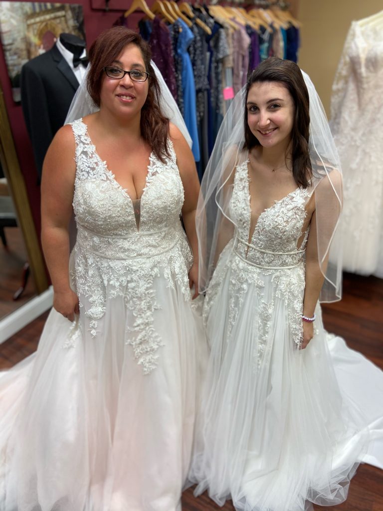 Lace V-neck dress on two brides into different sizes. Featured is the Rosa dress by Morilee in a size 6 and a size 18. Dress has lace straps, a double banded waist, and a layered tulle skirt