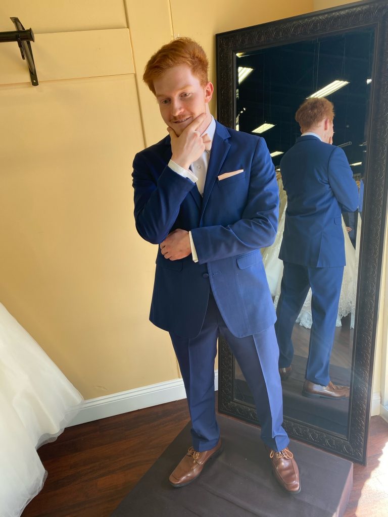 Groom trying on a cobalt blue tuxedo with a petal pink bowtie and matching pocket square, brown shoes, and white shirt