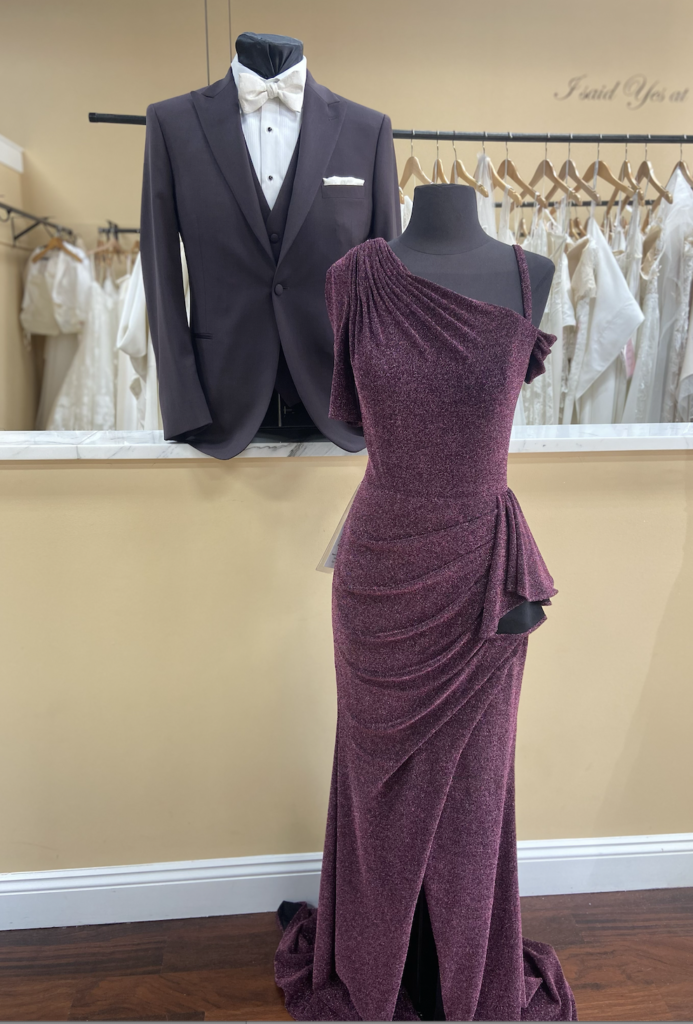 Mother of the bride dress in dark berry color on mannequin with one shoulder neckline, front rushing and side ruffle. Stretch jersey fabric with shimmer. 