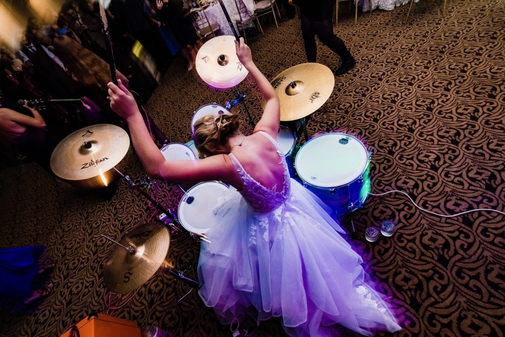Bride in her wedding dress playing the drums, Sarah is the drummer in the Philadelphia band Vixen77