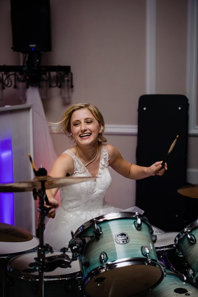 Sarah the bride playing the drums in her wedding dress at her reception