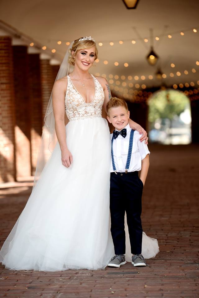 Darianna Bridal & Tuxedo bride Maggie in a wedding dress by Paloma Blanca alongside her ring bearer in suspenders and bow tie