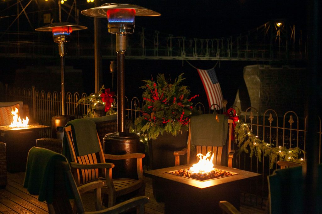 Riverside at the black bass hotel featuring heat lamps, fire pits, chairs with cozy blankets decorated for Christmas