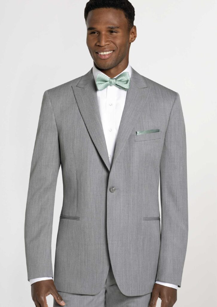 Gray suit on model, two-piece, jacket has peak, lapel, and one button close. Sage green bowtie and pocket square. White button-down shirt.