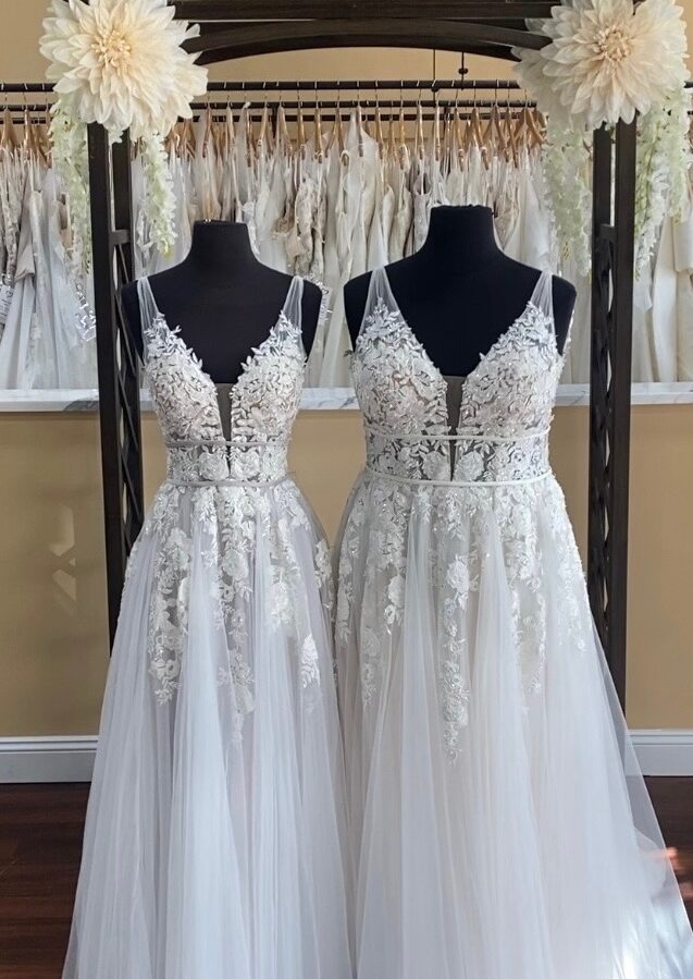 Two of the same wedding dresses on mannequins, one in a small size in a smoky lavender color with ivory lace, the other a plus size in all ivory.