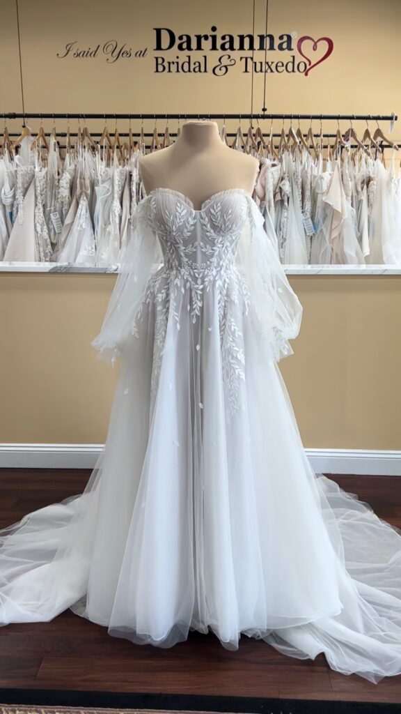 Essense of Australia D3787  on a mannequin at Darianna Bridal & Tuxedo, full front of wedding dress with sweetheart neckline, exposed boning construction in the bodice, soft a line skirt, vine lace, and off the shoulder, detachable bishop sleeves