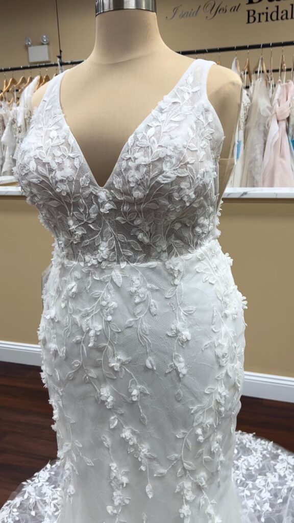 Fit and flare wedding dress on mannequin showing a vine lace lace pattern, V- neck in front, and side cut outs