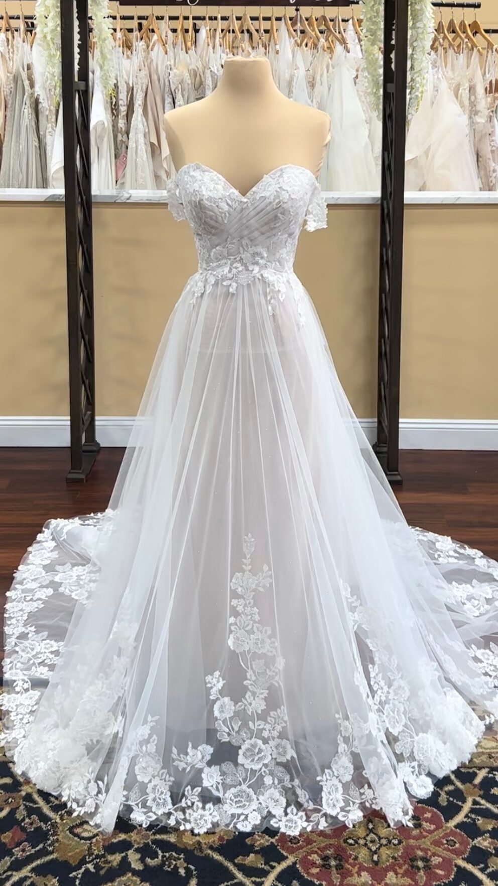 A-line wedding dress for apple shaped body type. Ruched sweetheart bodice with applique overlays, off the shoulder sleeves and  light tulle skirt with rose florets at the bottom.