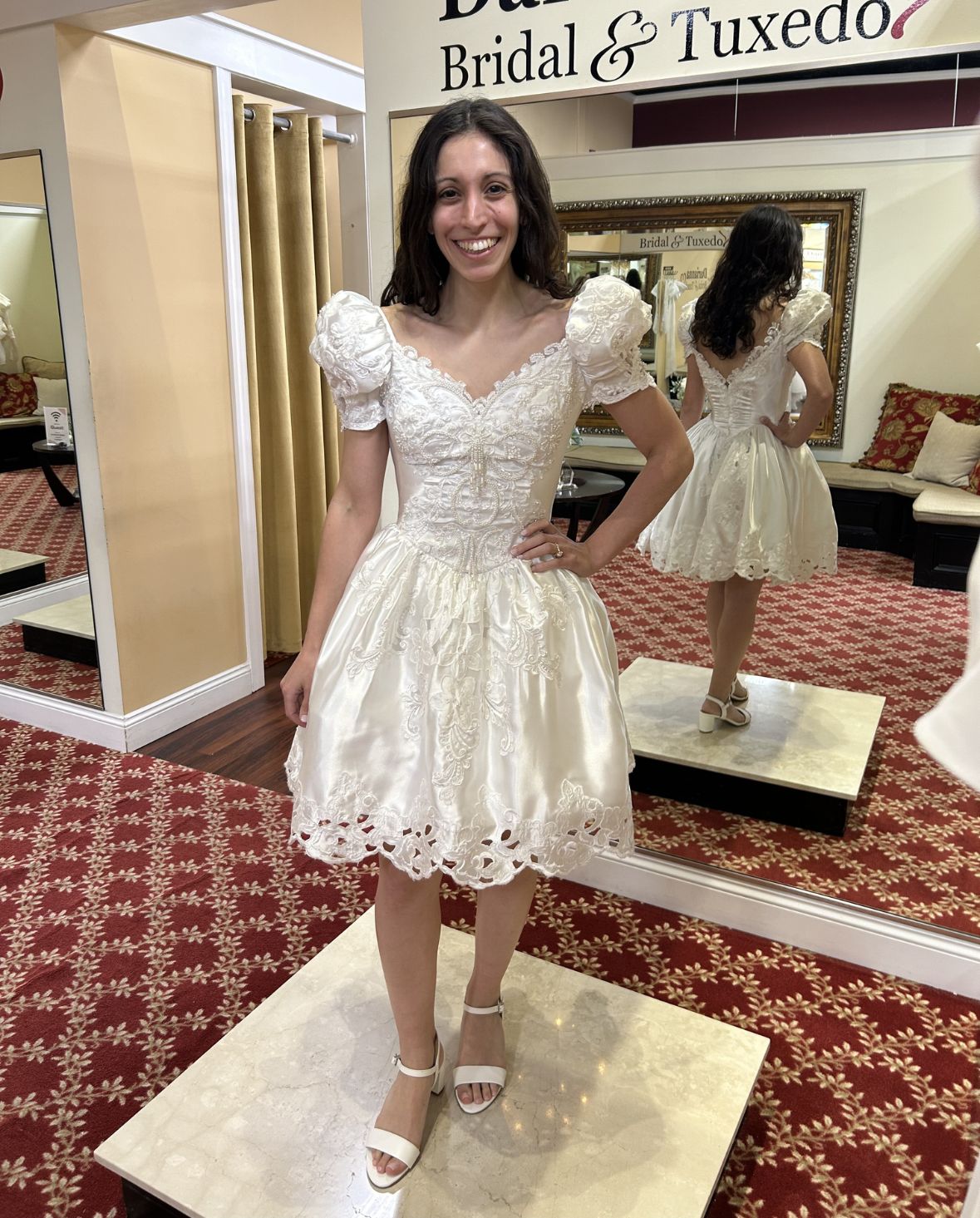Bride wearing a custom short lace wedding dress with puff sleeves during a bridal fitting